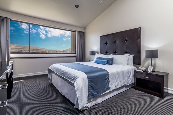 Habitación de hotel con una cama grande, una mesita de noche, un escritorio y una ventana con vistas al desierto.