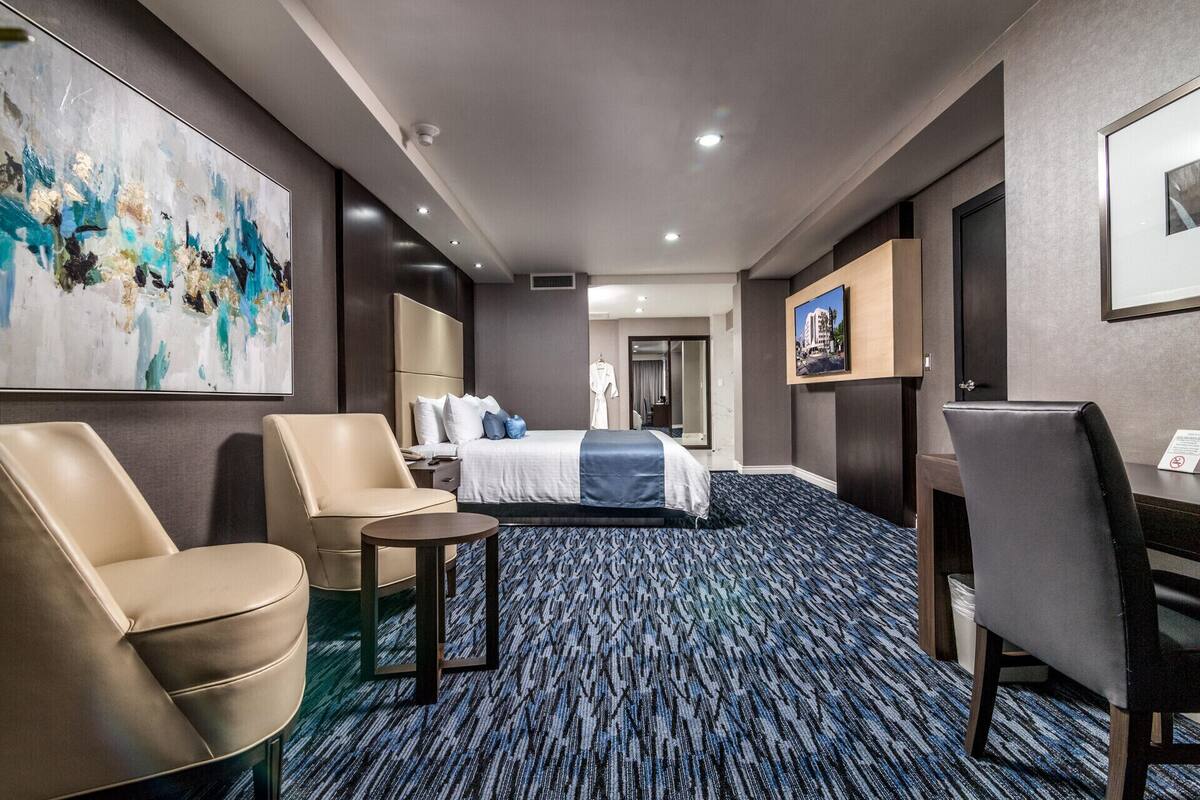 A hotel room with a bed, two chairs, a small table, a painting, and a mirror.