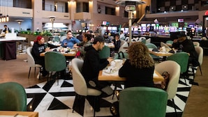 Un comedor con mesas y sillas, piso de cuadros y un edificio con balcones al fondo.