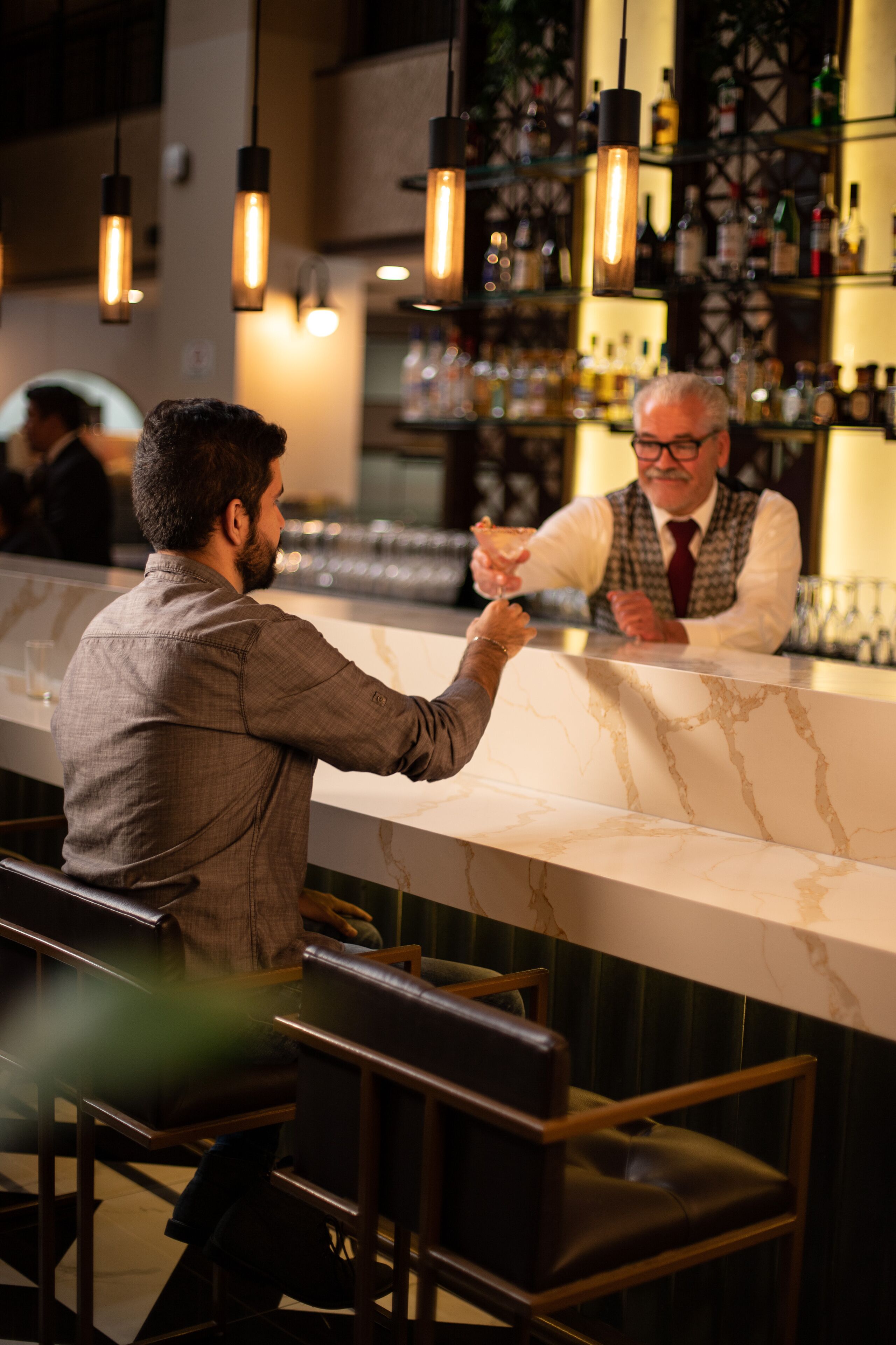 A bar area with a marble countertop and hanging pendant lights.