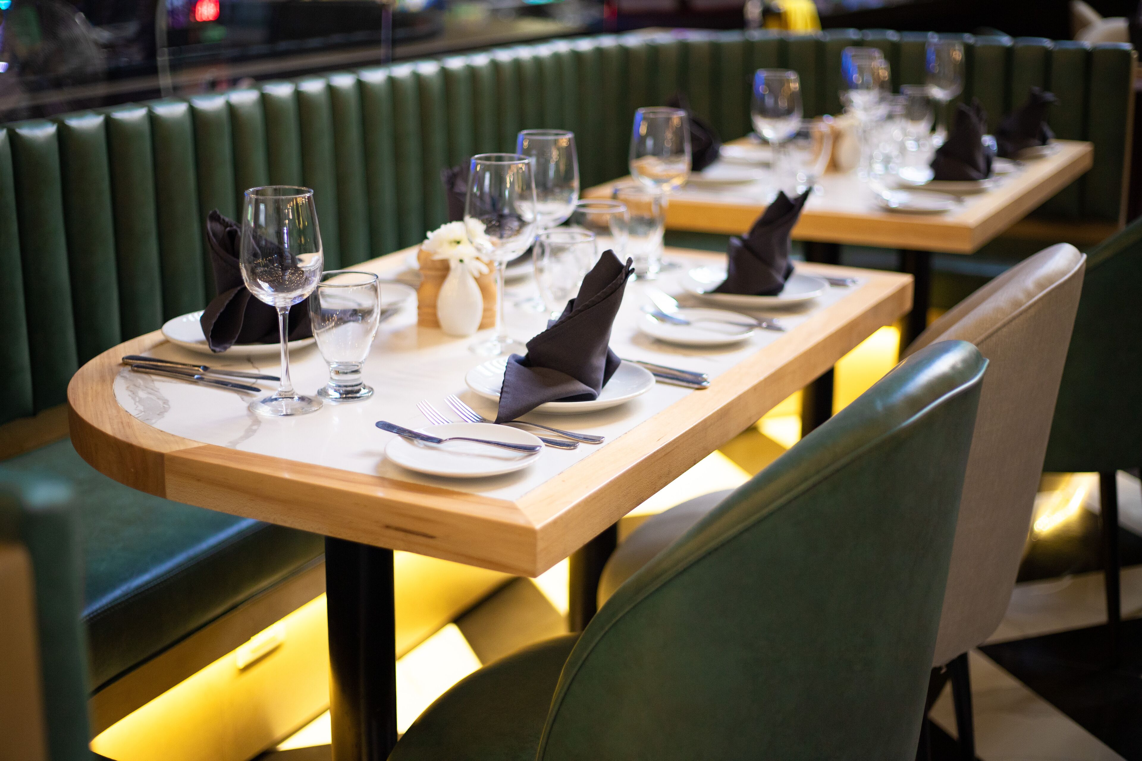 Un restaurante con asientos tapizados en verde, mesas de madera dispuestas con platos, vasos y cubiertos.