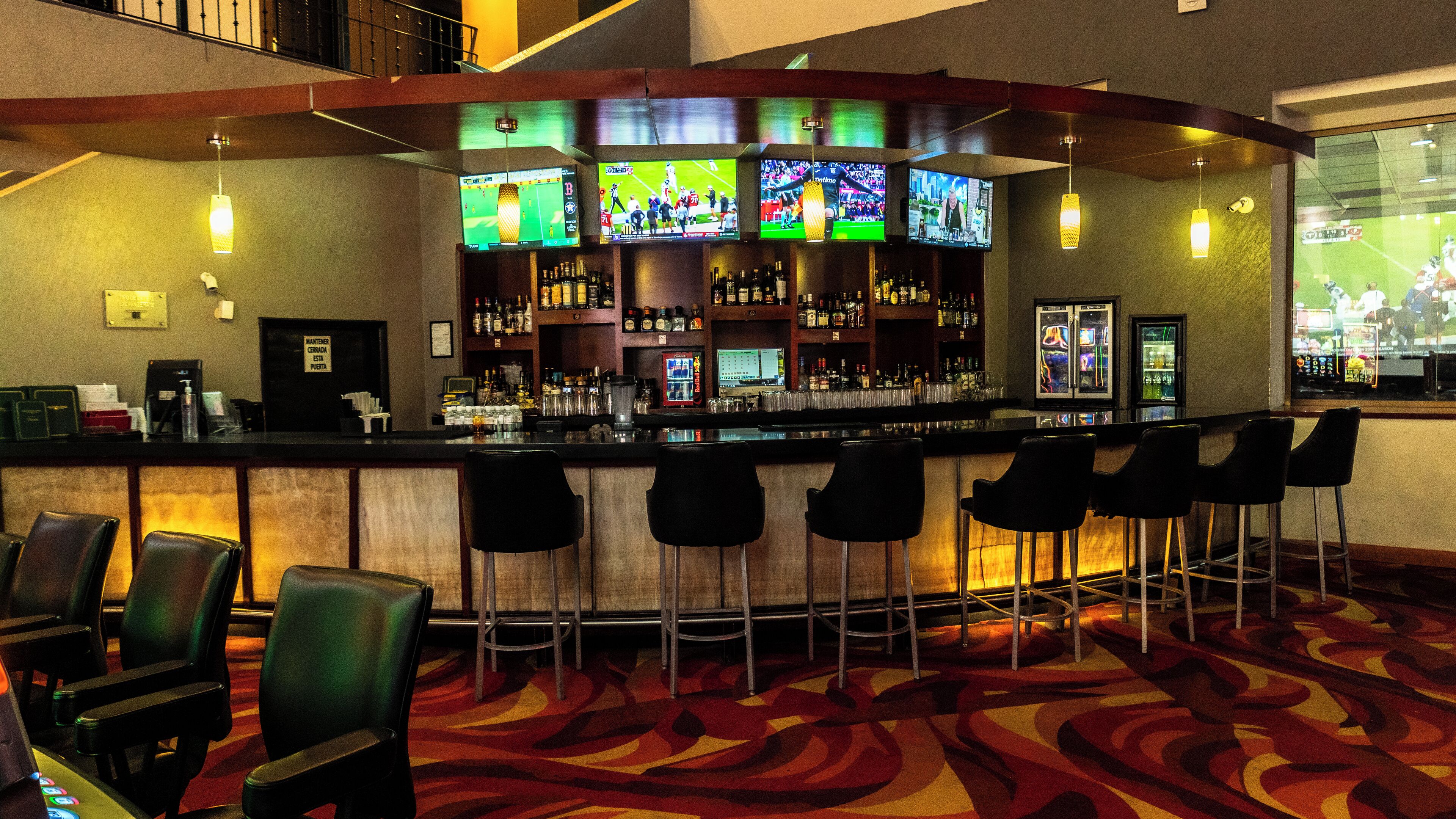 A bar area with multiple TVs, a bar counter, and several bar stools.