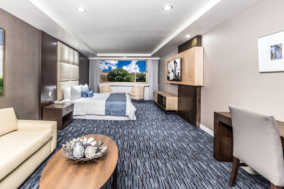 A hotel room with a bed, a sofa, a coffee table, and a desk.