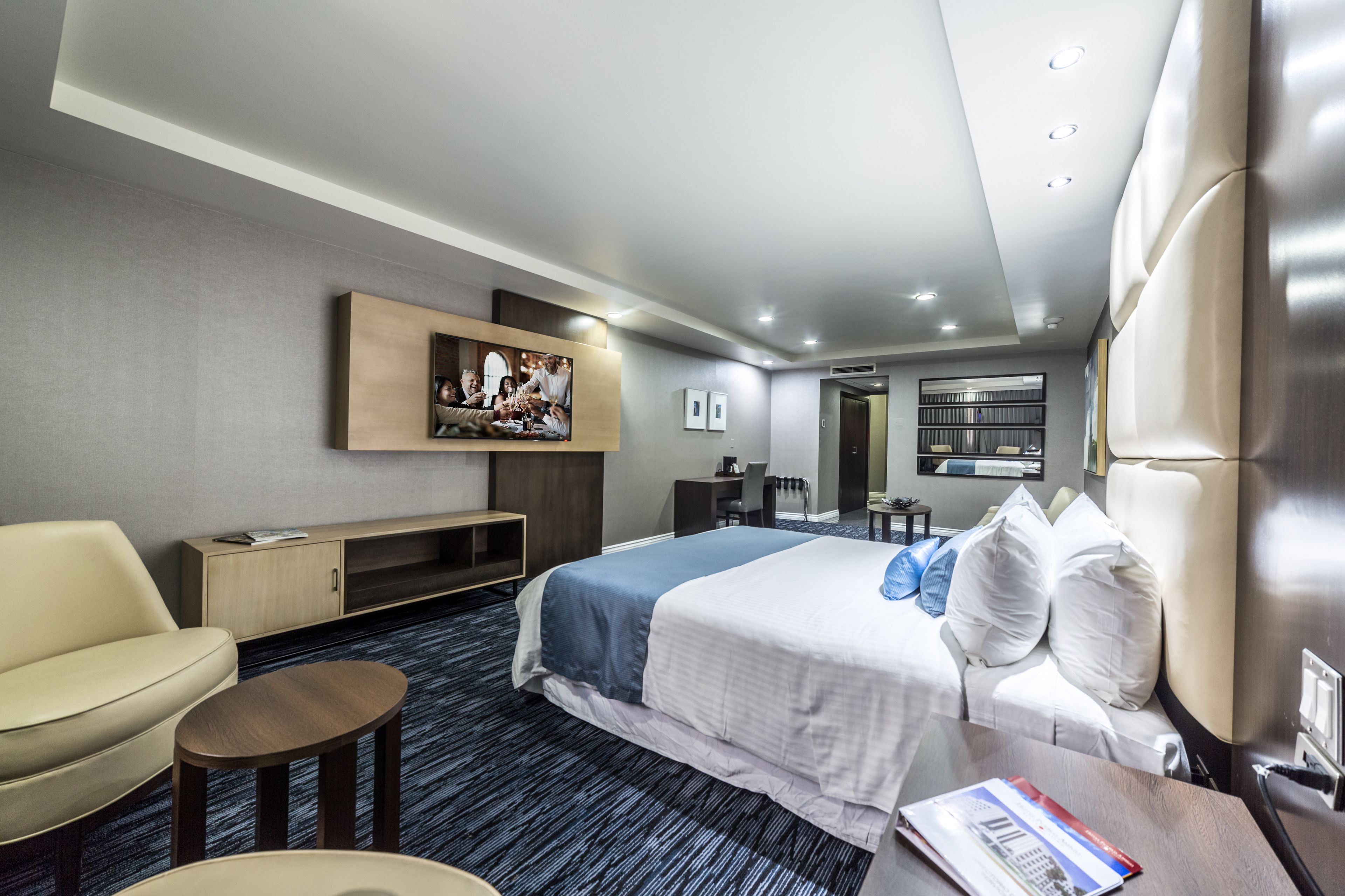 Une chambre d’hôtel moderne avec un grand lit, un canapé, une petite table, un téléviseur fixé au mur et une bibliothèque.