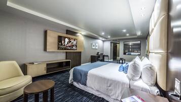 Une chambre d’hôtel moderne avec un grand lit, un canapé, une petite table, un téléviseur fixé au mur et une bibliothèque.