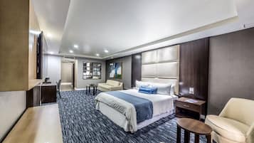 A modern hotel room with a large bed, a desk, a chair, a small table, and a TV.