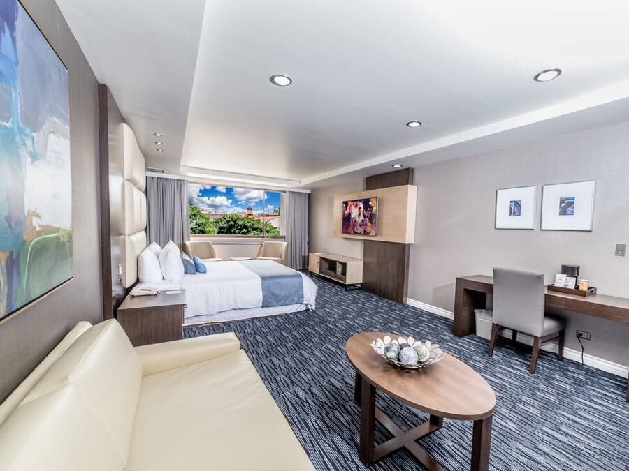 Moderni hotellihuone, jossa on suuri sänky, työpöytä, tuoli ja pieni pöytä.