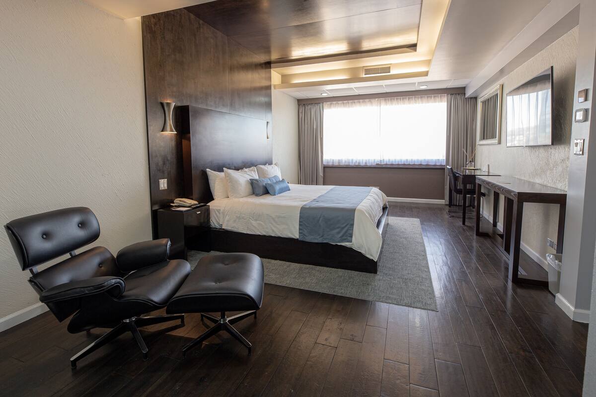 A modern hotel room with a large bed, a desk, and a seating area.