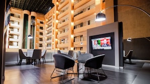 Un moderno vestíbulo de hotel con comedor, una pantalla de televisión mostrando un noticiero y vistas de los balcones interiores del edificio.