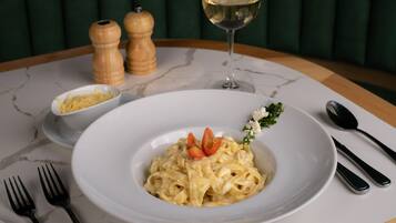 Una mesa de comedor con un plato de pasta, una copa de vino blanco, saleros y pimenteros, y cubiertos.