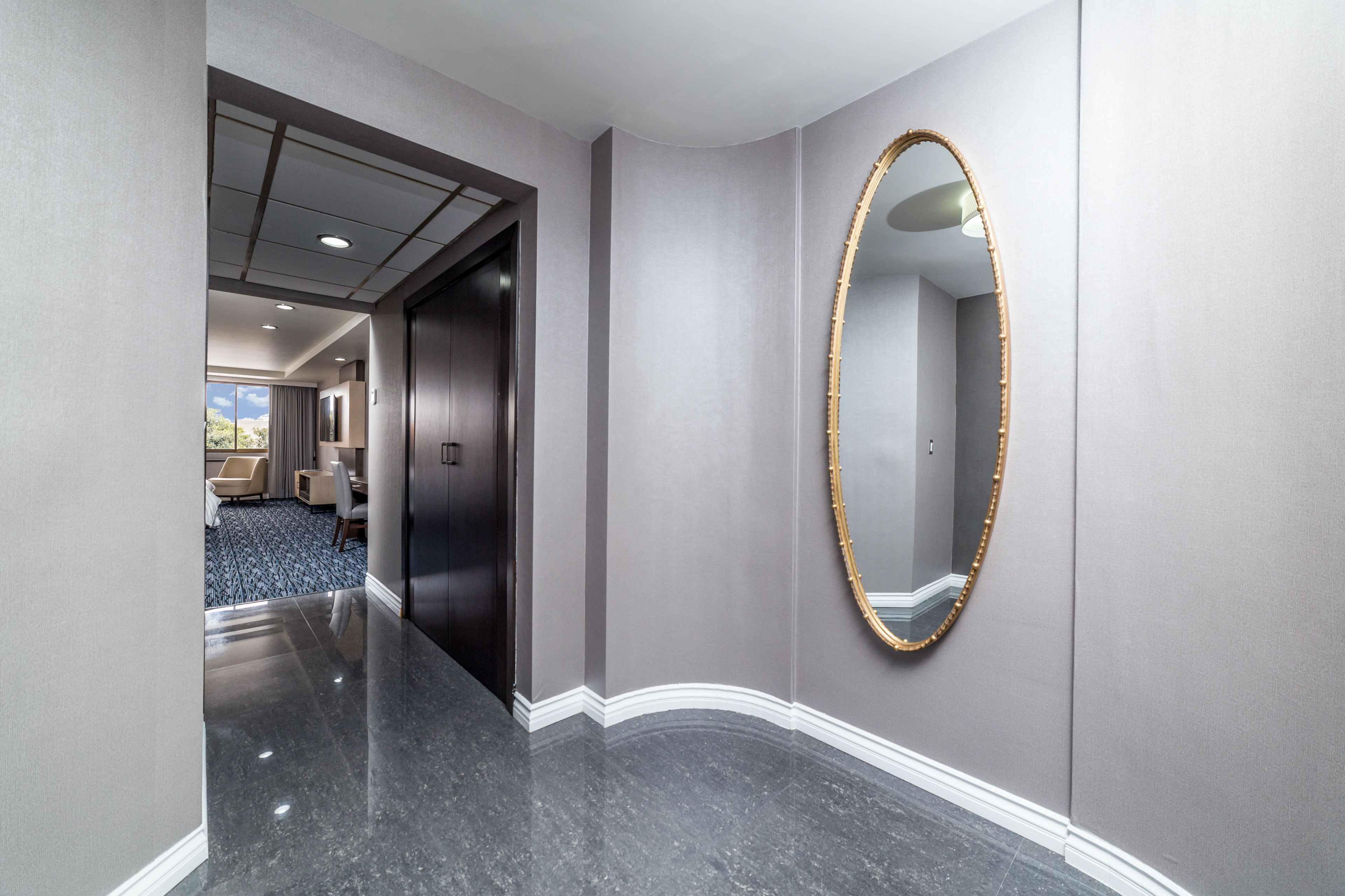 A hallway with a marble floor, a large mirror with a gold frame, and a door leading to a room with a view of the outdoors.