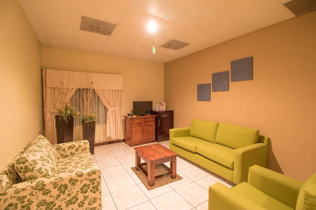 Una sala de estar con un sofá floral, un sofá verde, una mesa de centro de madera y un mueble con televisor.