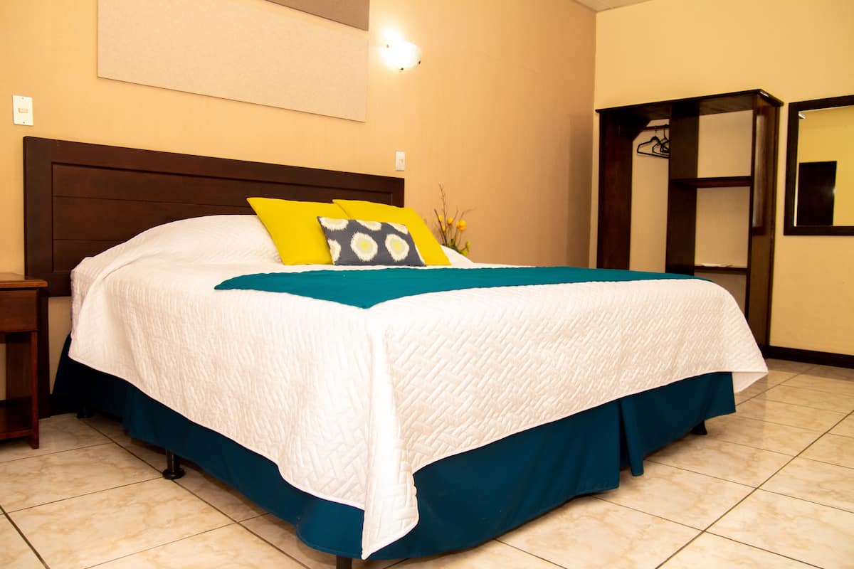 Una cama bien tendida con una colcha blanca y azul verdosa, un cabecero de madera y una mesita de noche con una lámpara.