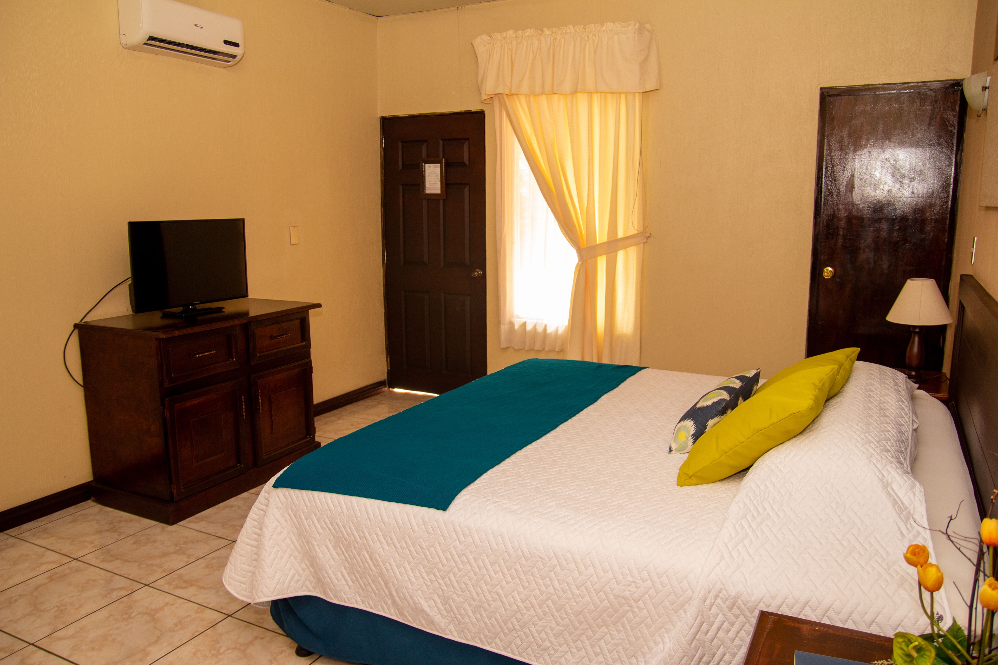 A hotel room with a bed, a television on a wooden cabinet, a door, and a window with curtains.
