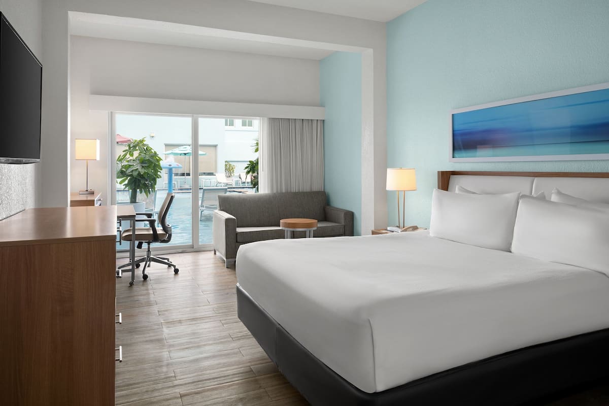 A hotel room with a large bed, a desk, a chair, a small table, and a TV.