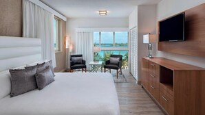 A hotel room with a large bed, a TV mounted on the wall, a desk with two chairs, and a view of the ocean. - Courtyard by Marriott Nassau Downtown/Junkanoo Beach (Nassau)