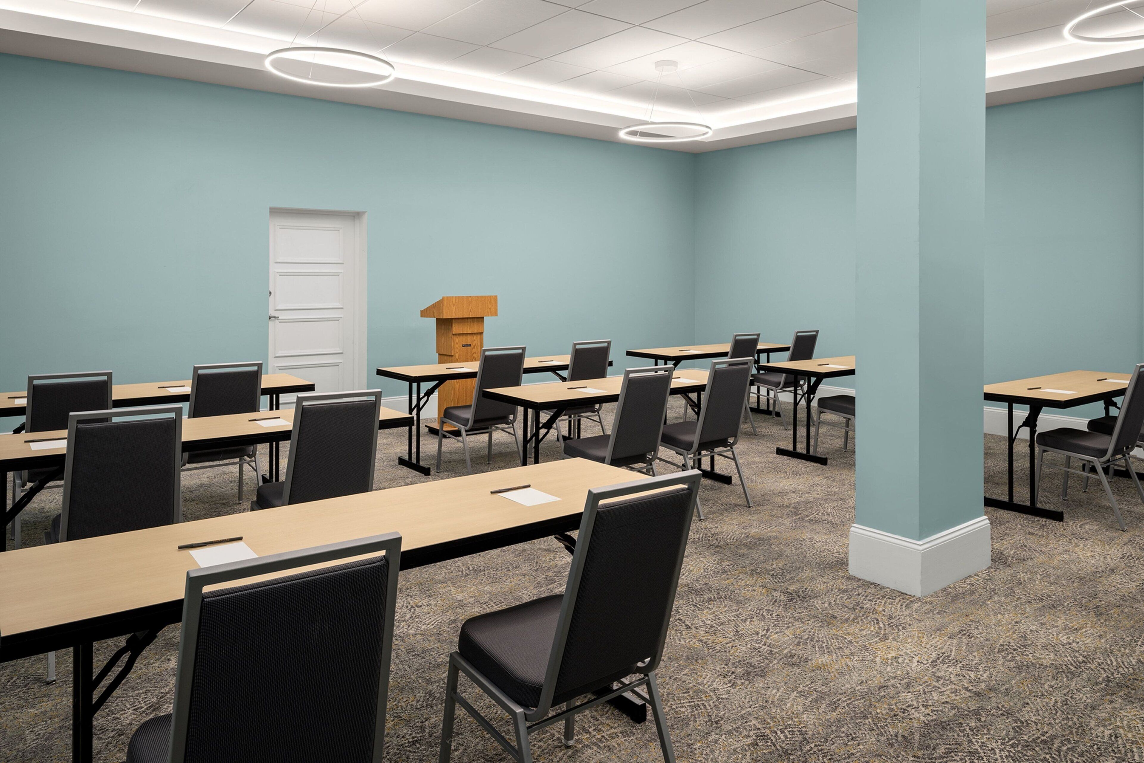 A conference room with multiple tables and chairs, a podium, and a door.