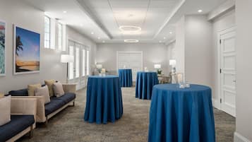 Un vestíbulo de hotel con alfombra azul, un sofá con cojines y mesas redondas cubiertas con manteles azules.