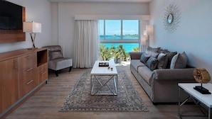 A modern living room with a flat-screen TV, a coffee table, a sofa, and a large window offering a view of the ocean. - Courtyard by Marriott Nassau Downtown/Junkanoo Beach (Nassau)