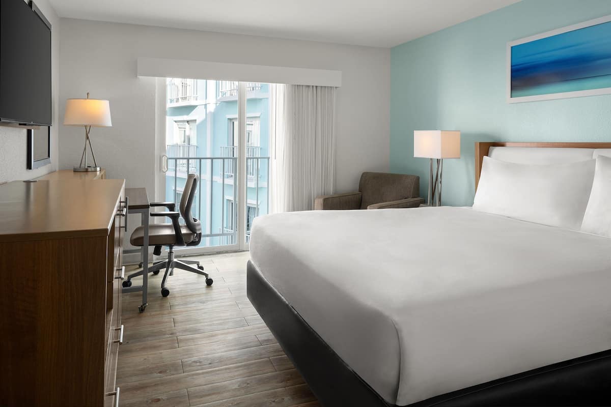 A hotel room with a bed, desk, chair, and a TV.
