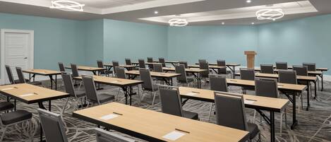 A conference room with multiple tables and chairs, a podium, and a carpeted floor.