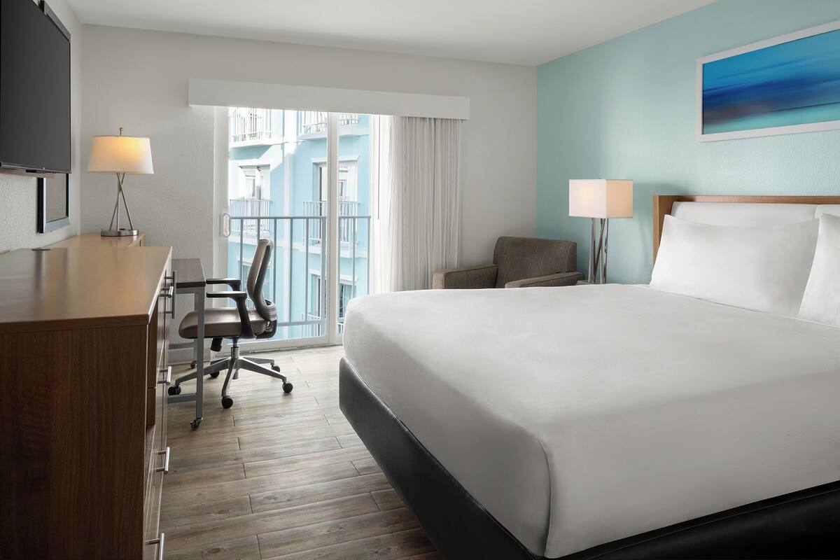 A hotel room with a bed, desk, chair, and two lamps.