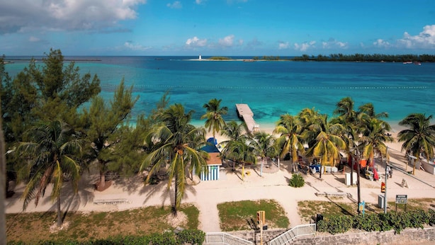 A beach with palm trees, a pier, and a lighthouse in the distance. - Courtyard by Marriott Nassau Downtown/Junkanoo Beach (Nassau)