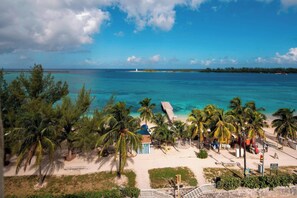 A beach with palm trees, a pier, and a lighthouse in the distance. - Courtyard by Marriott Nassau Downtown/Junkanoo Beach (Nassau)