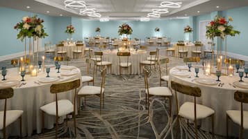 Un salón de banquetes con mesas redondas, sillas y centros de mesa florales.