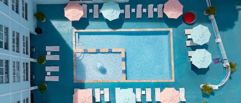 An aerial view of a hotel pool area with multiple lounge chairs, umbrellas, and a central swimming pool.