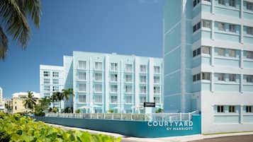 Un hotel de diverses plantes amb façana de blau clar, una zona de pati amb seients a l'aire lliure i un cartell visible que diu "Courtyard by Marriott".