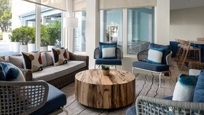 A modern living room with a round wooden coffee table, wicker furniture, and large windows offering a view of the city. - Courtyard by Marriott Nassau Downtown/Junkanoo Beach (Nassau)