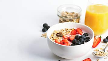 A bowl of cereal with strawberries and blueberries, a glass of orange juice, and a jar of granola.