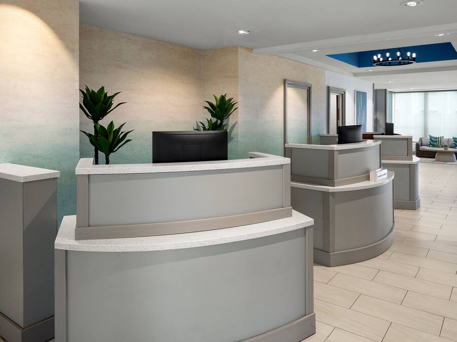 A reception area with a modern design, featuring a central reception desk, two potted plants, and a seating area with sofas and a coffee table.