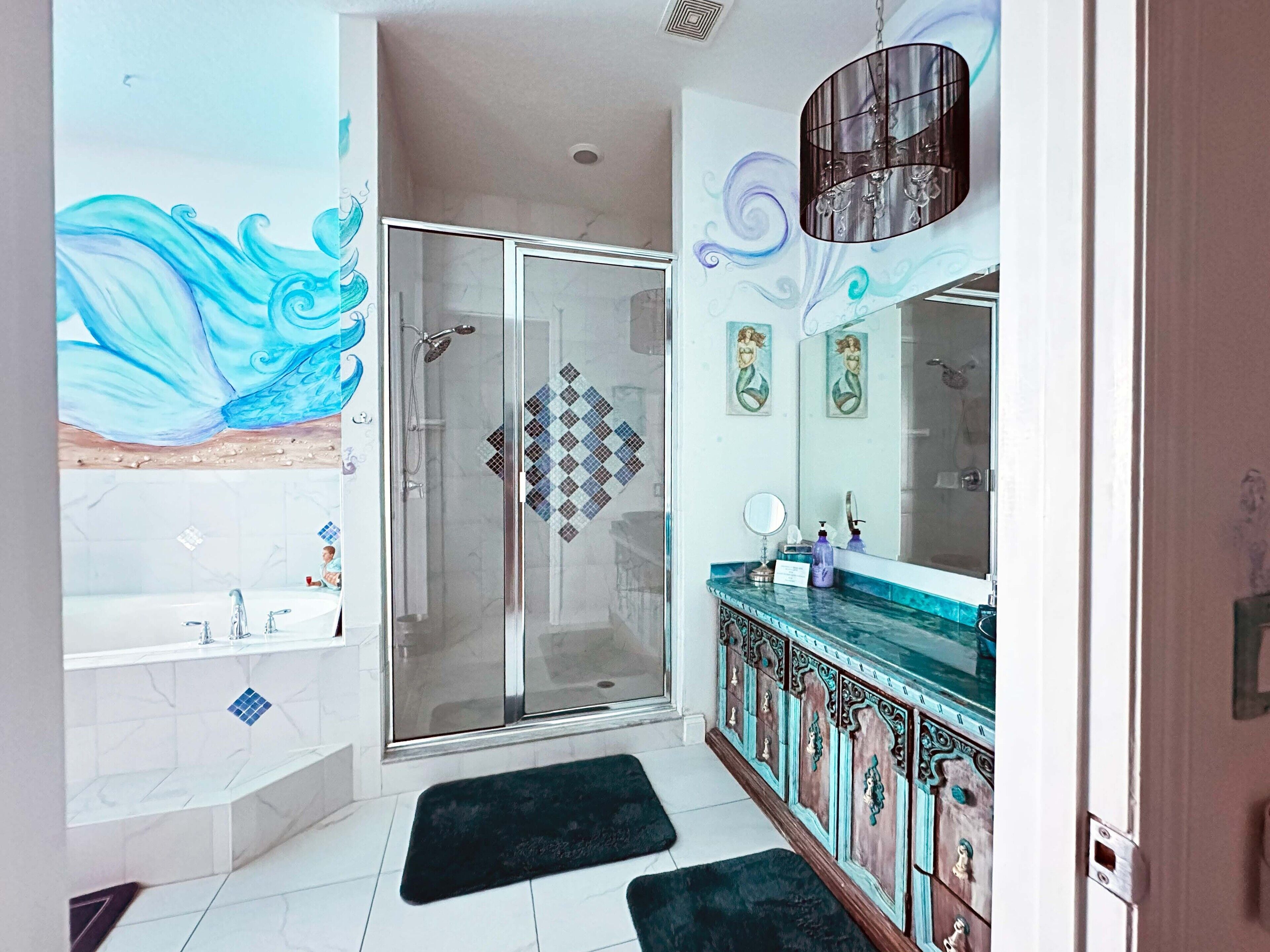 Une salle de bain moderne dotée d’une douche à parois de verre, d’un meuble-lavabo agrémenté d’un miroir décoratif et d’une grande fresque murale.
