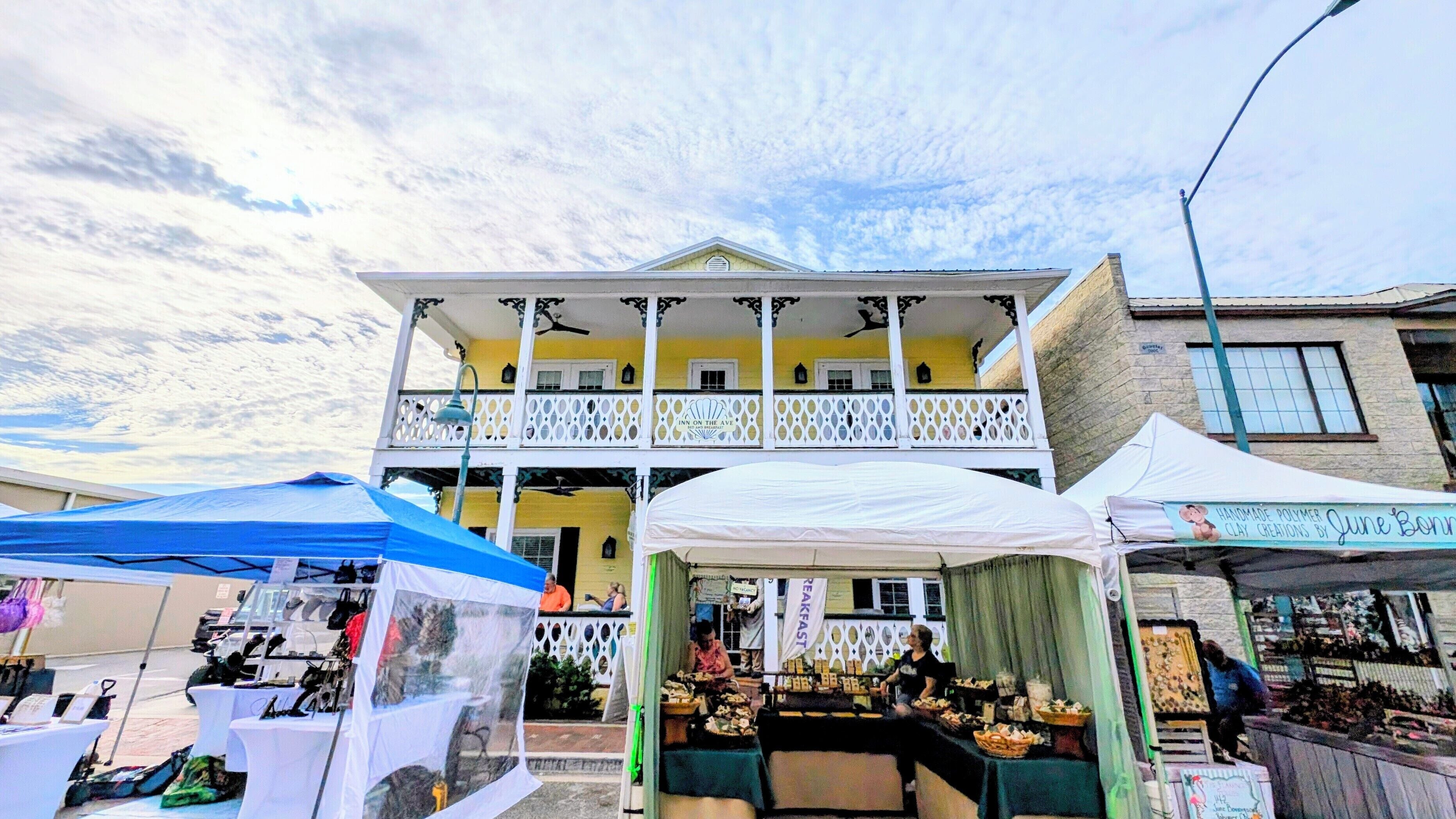 Un bâtiment à deux étages doté d’un balcon, d’une enseigne indiquant « Inn on the Ave », et d’un étal de marché où sont vendus divers articles.