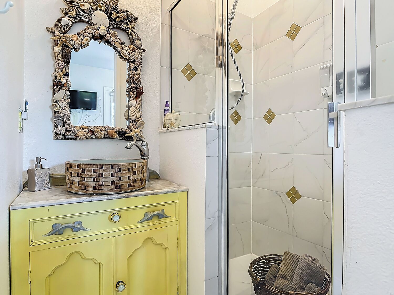 Un baño con tocador amarillo, un lavabo redondo con diseño de mosaico, un espejo decorativo y una ducha con azulejos de patrón de diamante.
