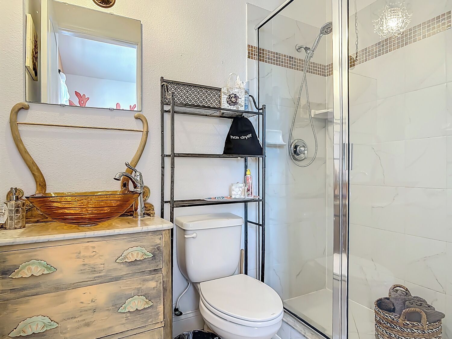 Ein Badezimmer mit Holzwaschtisch, Toilette in Weiß, einer Duschkabine aus Glas und einem Metallregal mit Pflegeprodukten.