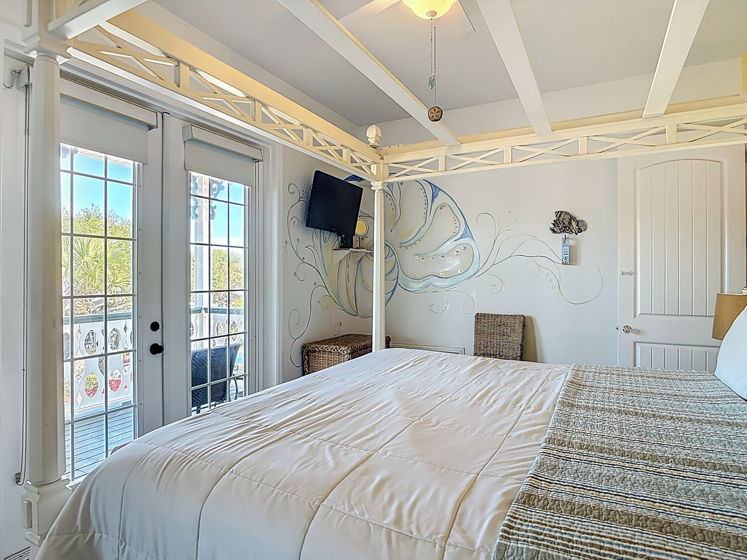 A bedroom with a large bed, a television mounted on the wall, a door leading to a balcony, and a decorative wall mural.