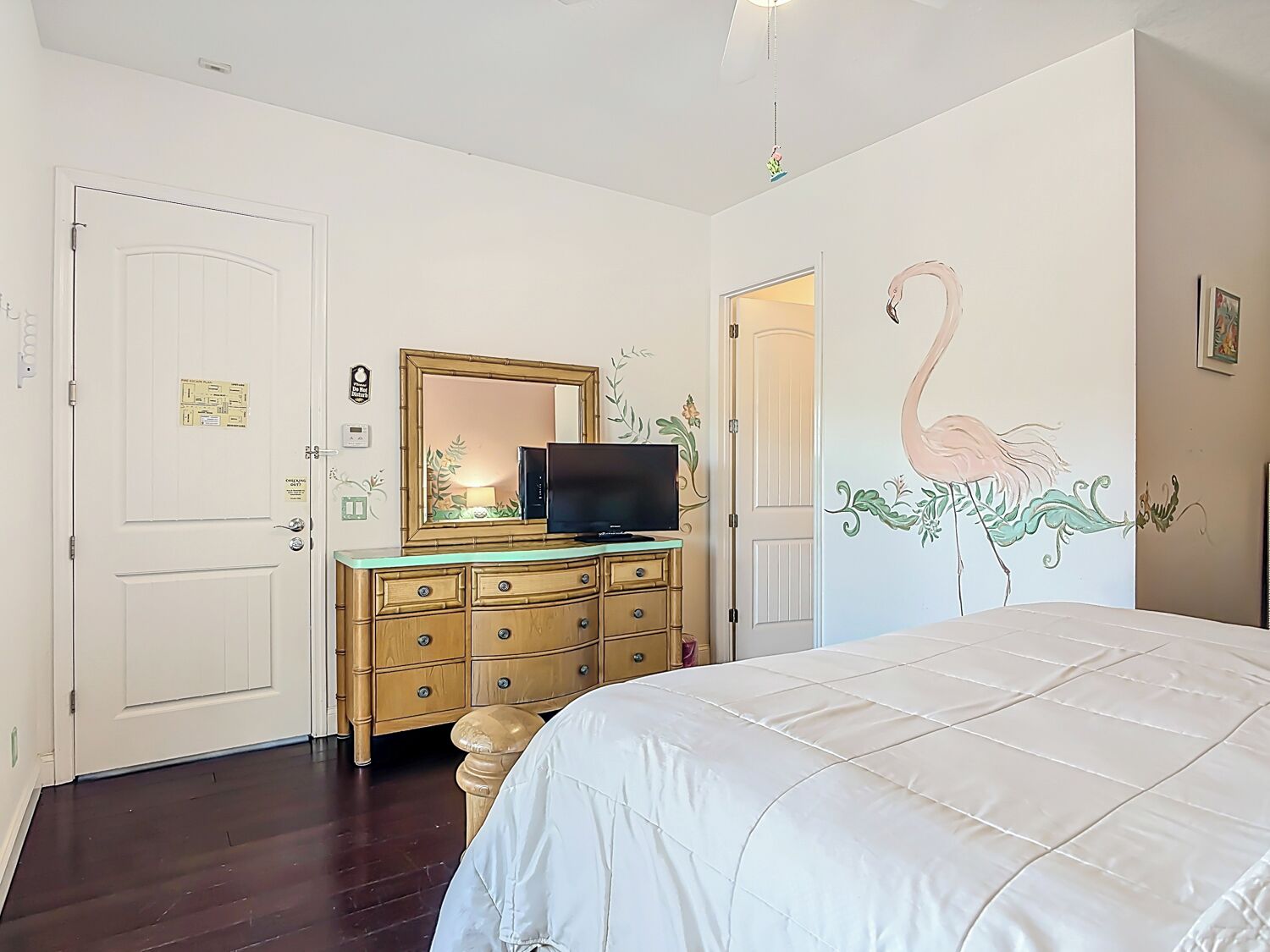 A bedroom with a bed, a dresser, a television, and a wall mural.