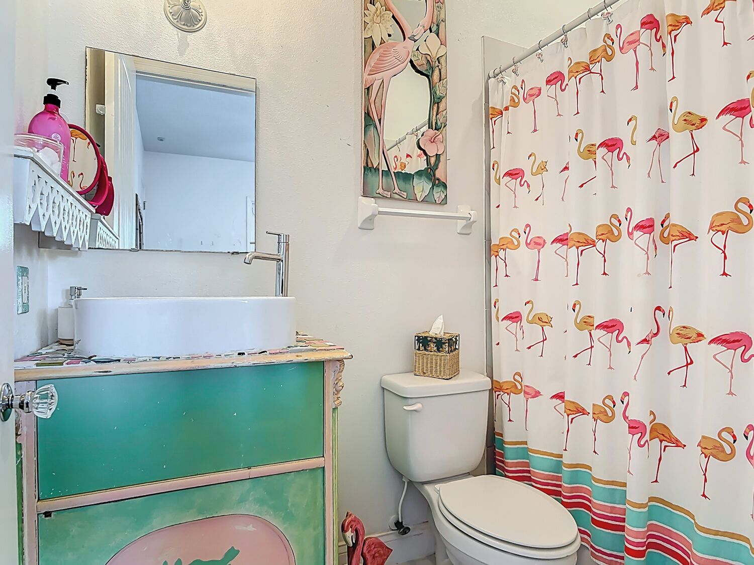 A bathroom with a white sink, a green vanity, a toilet, and a shower curtain with flamingo prints.