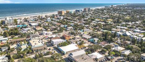 An aerial view of a coastal town with a dense cluster of buildings, a beach, and a clear blue sky.