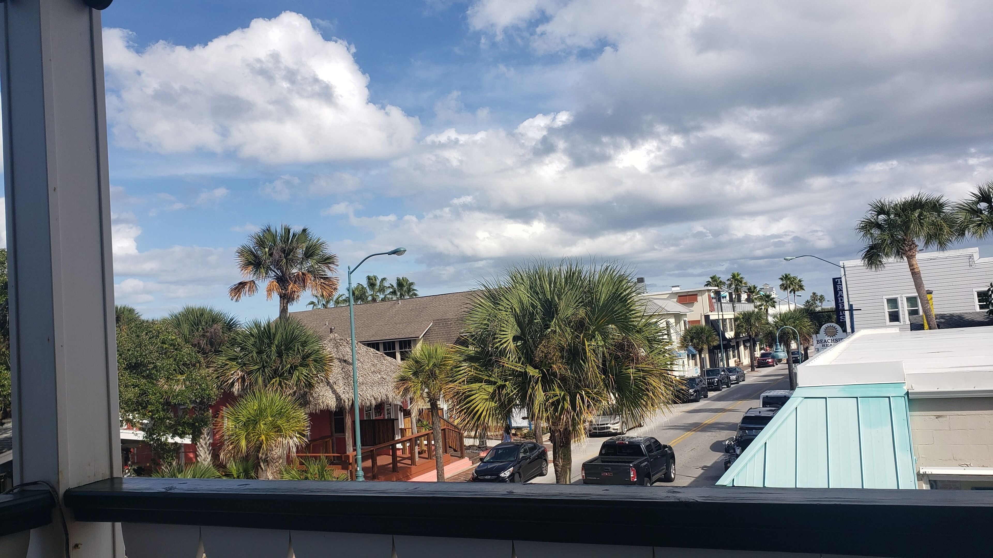 A street view with palm trees, a building with a sign reading "TRADES", and a beachside restaurant.