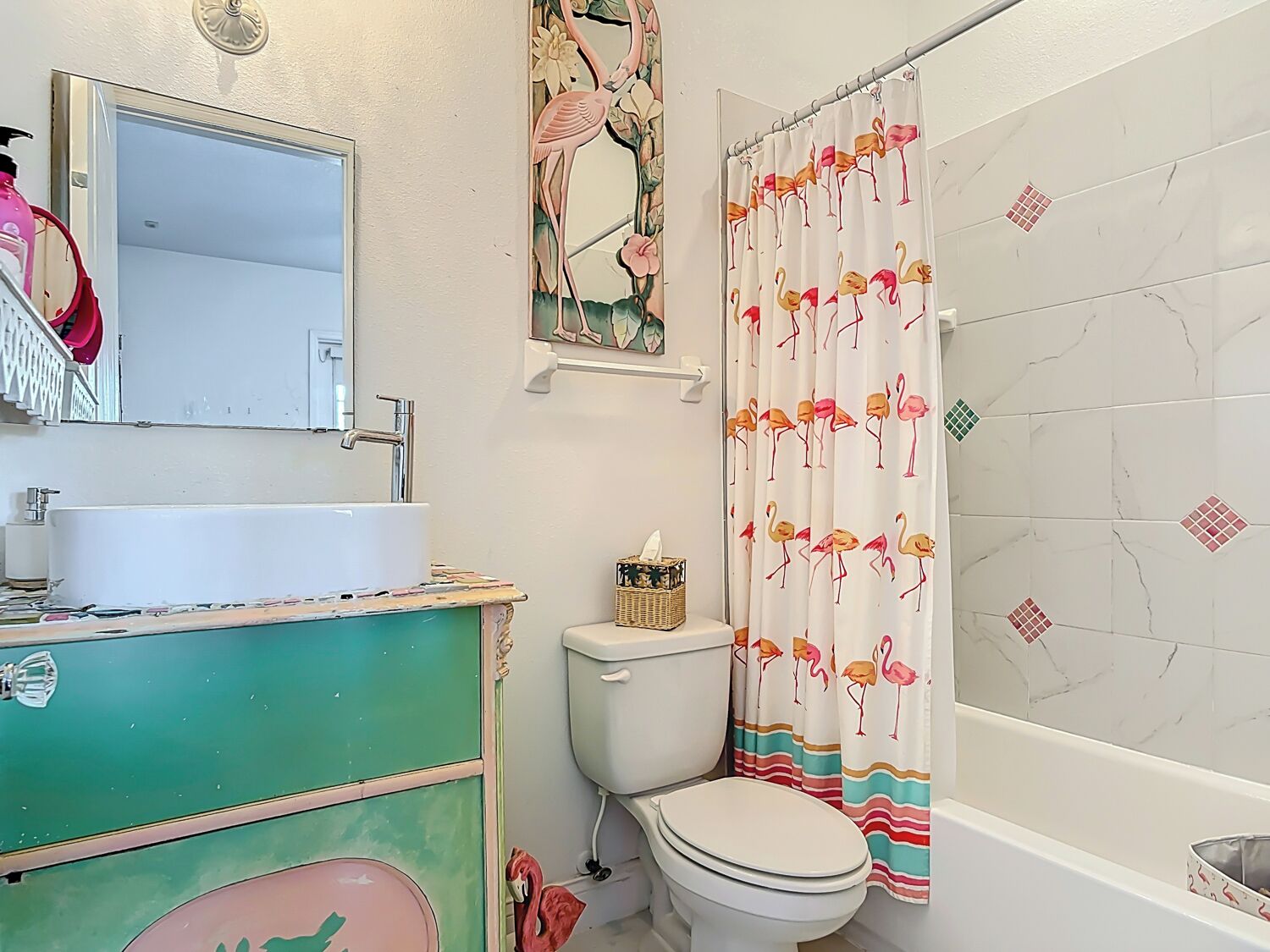 A bathroom with a white sink, a toilet, and a shower curtain with a flamingo pattern.