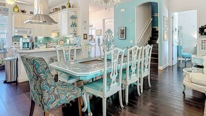 Una cocina amplia con armarios blancos, un comedor con una mesa y sillas estampadas, y una araña.