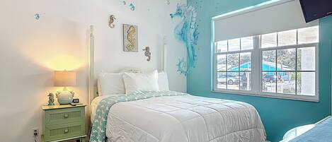 A bedroom with a bed, a nightstand, a dresser, a window with a view, and a ceiling fan.