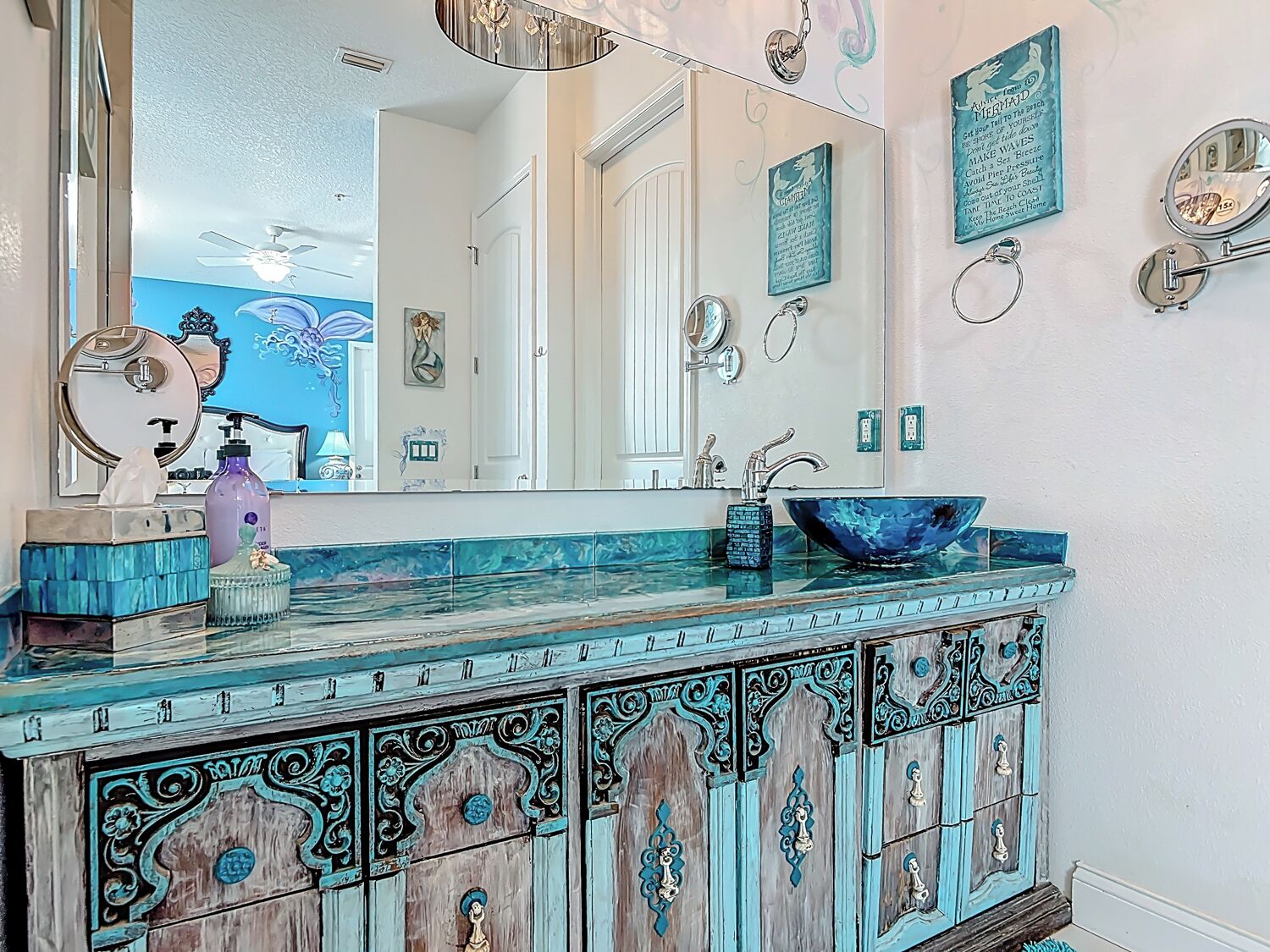 Un baño con un espejo grande, un lavamanos azul y un mueble decorativo con diseños elaborados.
