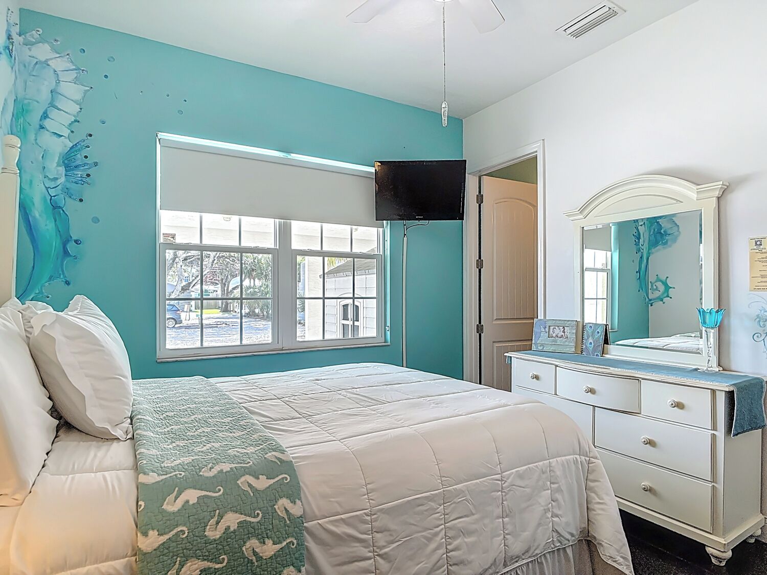 A bedroom with a bed, a dresser, a mirror, and a window with a view of the outside.