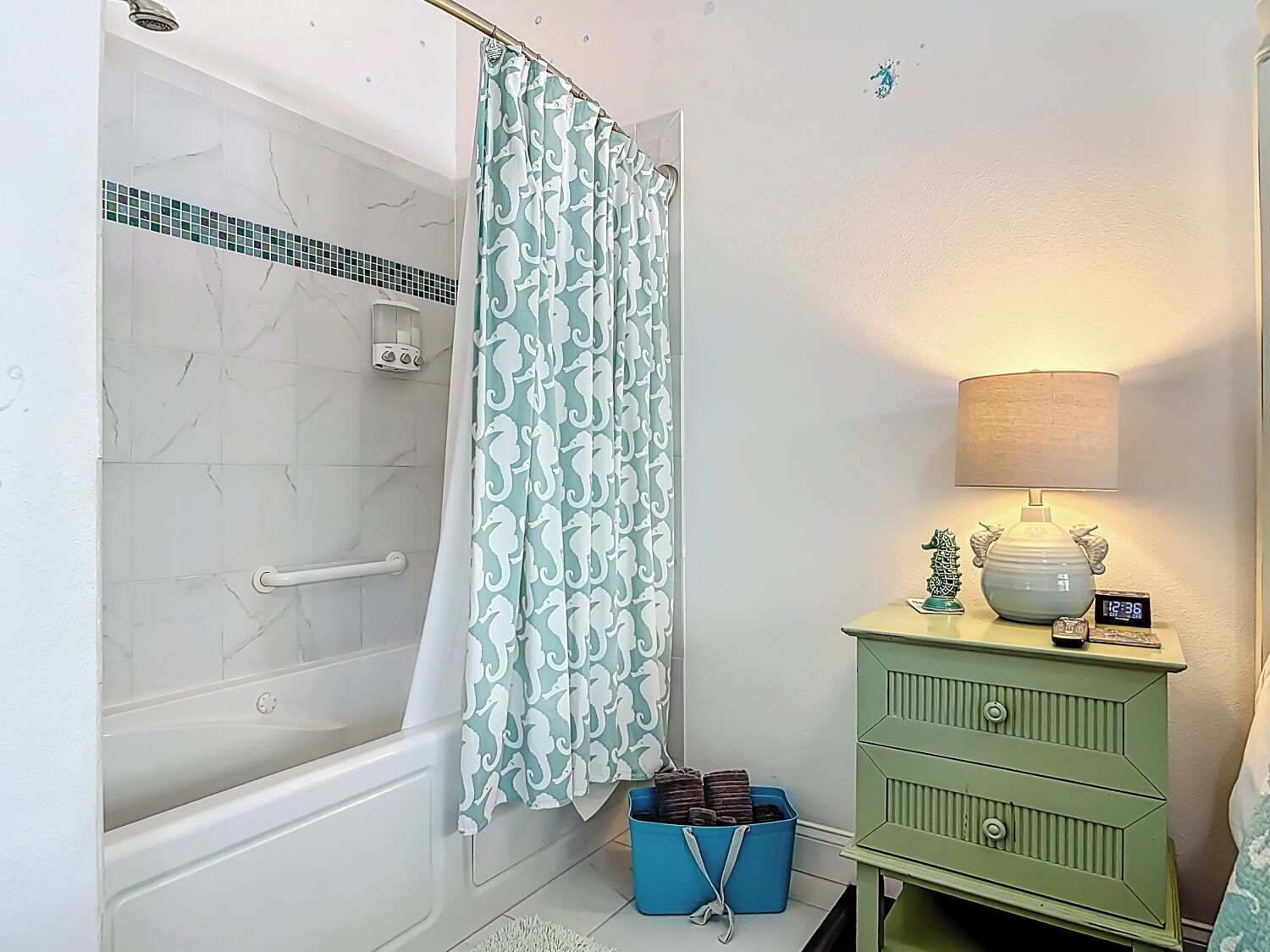 Une salle de bain avec une douche, un meuble-lavabo vert, un bac de rangement bleu et une lampe fixée au mur.
