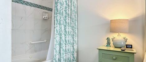 Un baño con ducha, un tocador verde, un contenedor azul para guardar objetos y una lámpara fijada a la pared.